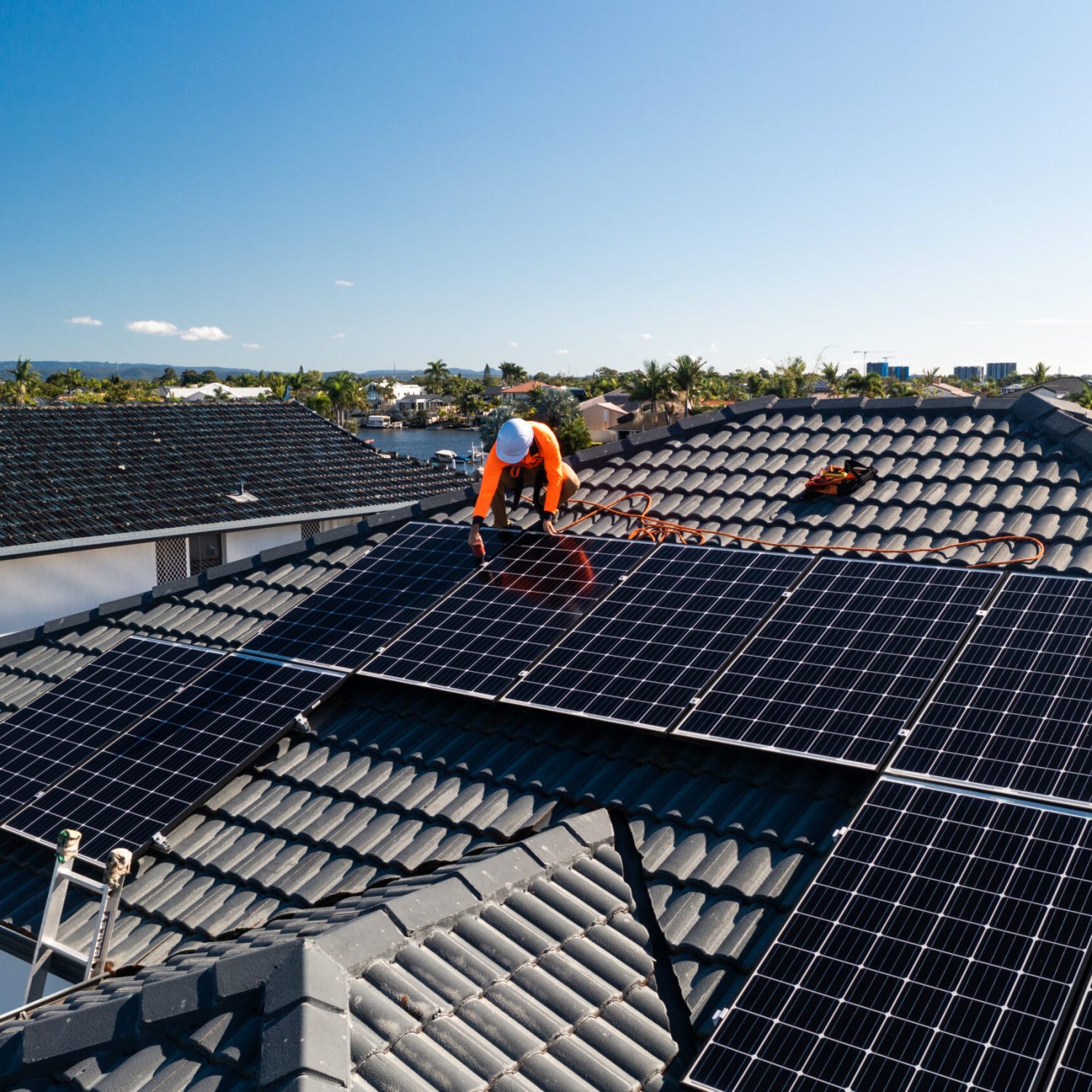 Solar panels and technician on luxury waterfront home on a sunny day.